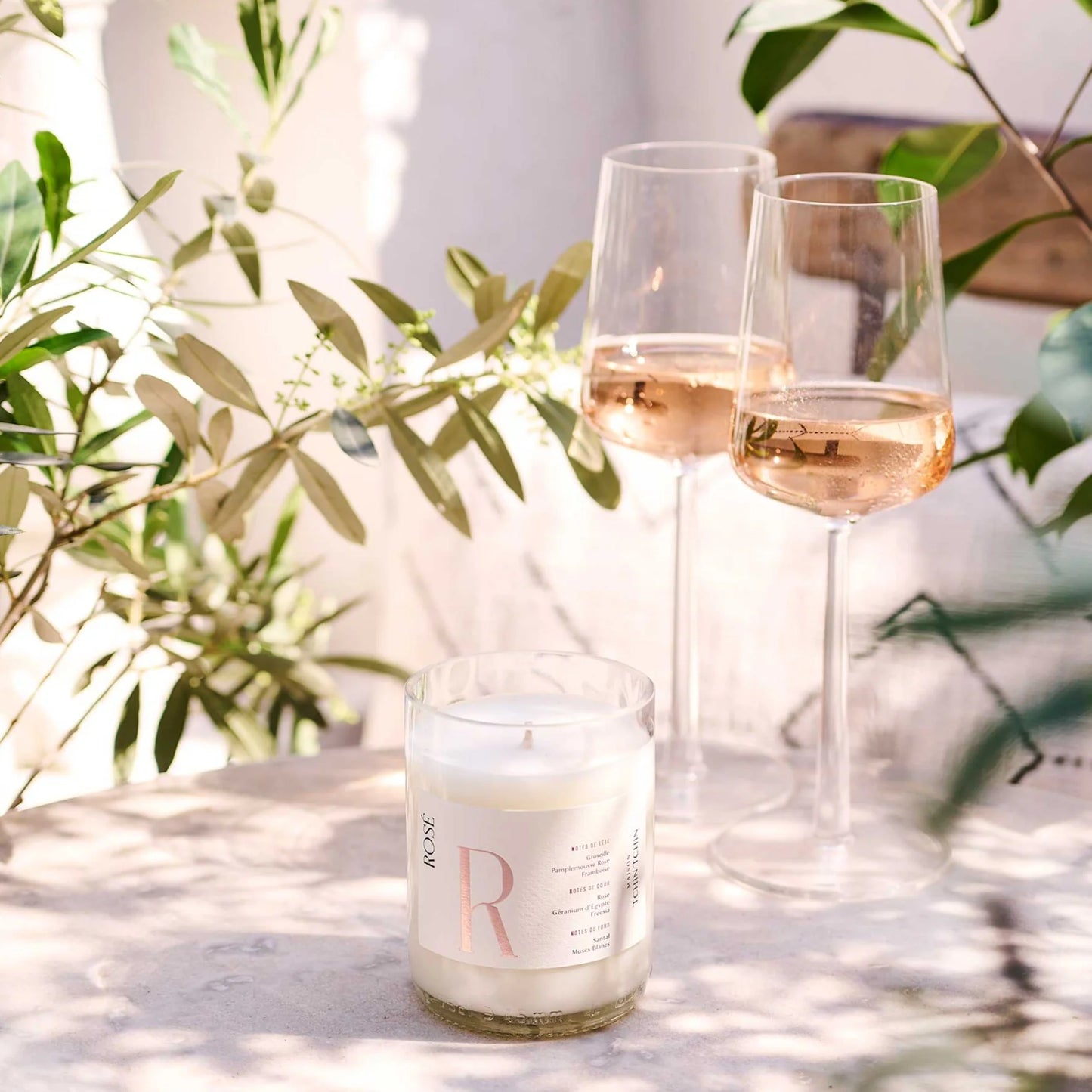 Bougies parfumée au rosé Maison Tchin Tchin posée sur une table de jardin avec deux verres de rosé à côté