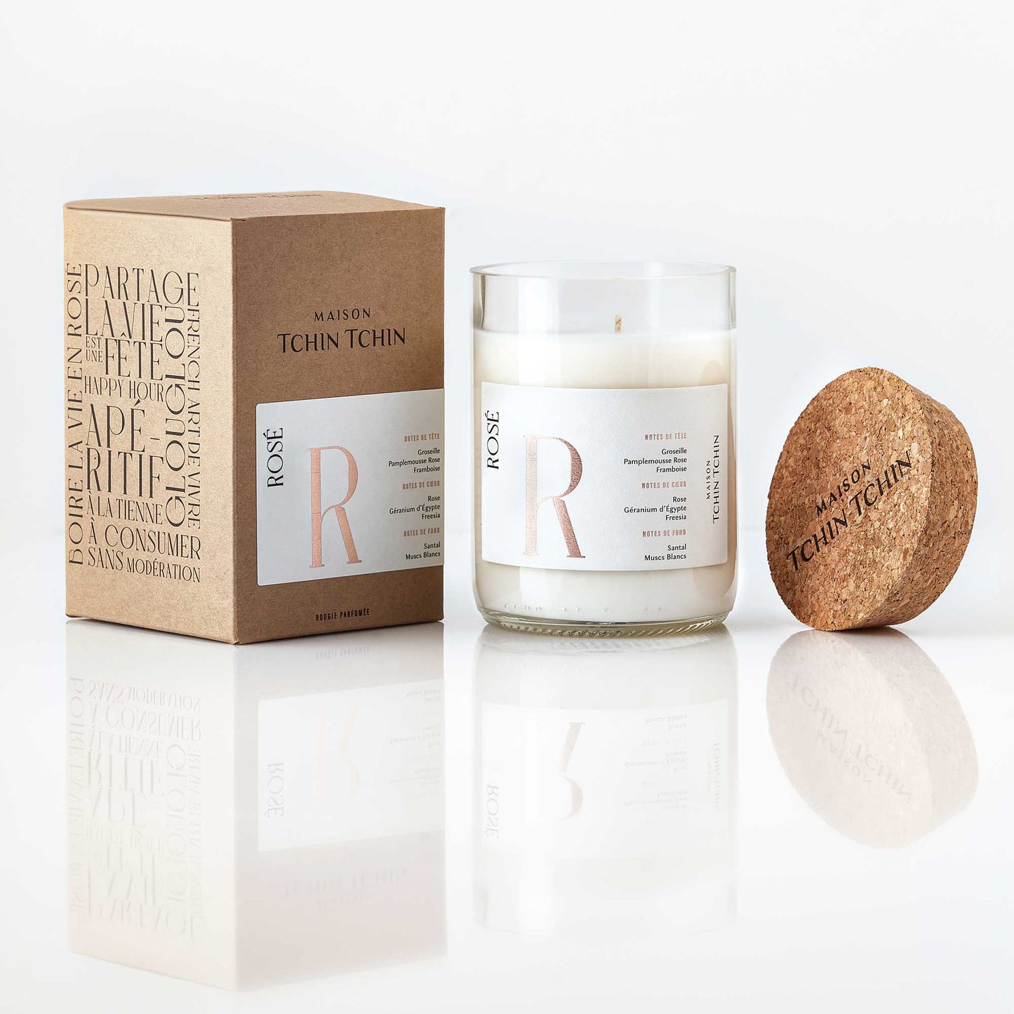 Maison Tchin Tchin Bougie parfumée au rosé posée sur un fond blanc avec sa boîte en carton recyclé.