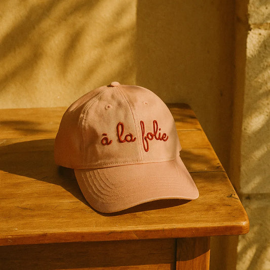 Casquette rose pour femme brodée A la Folie posée sur une table en bois.