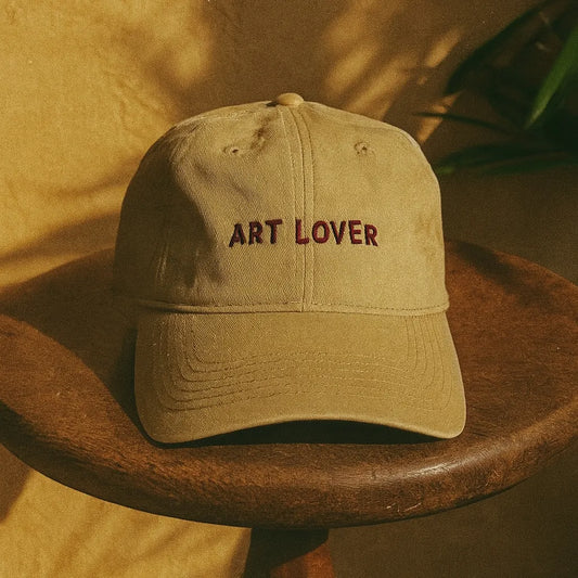 Casquette beige brodée avec message Art Lover, posée sur une table en bois.