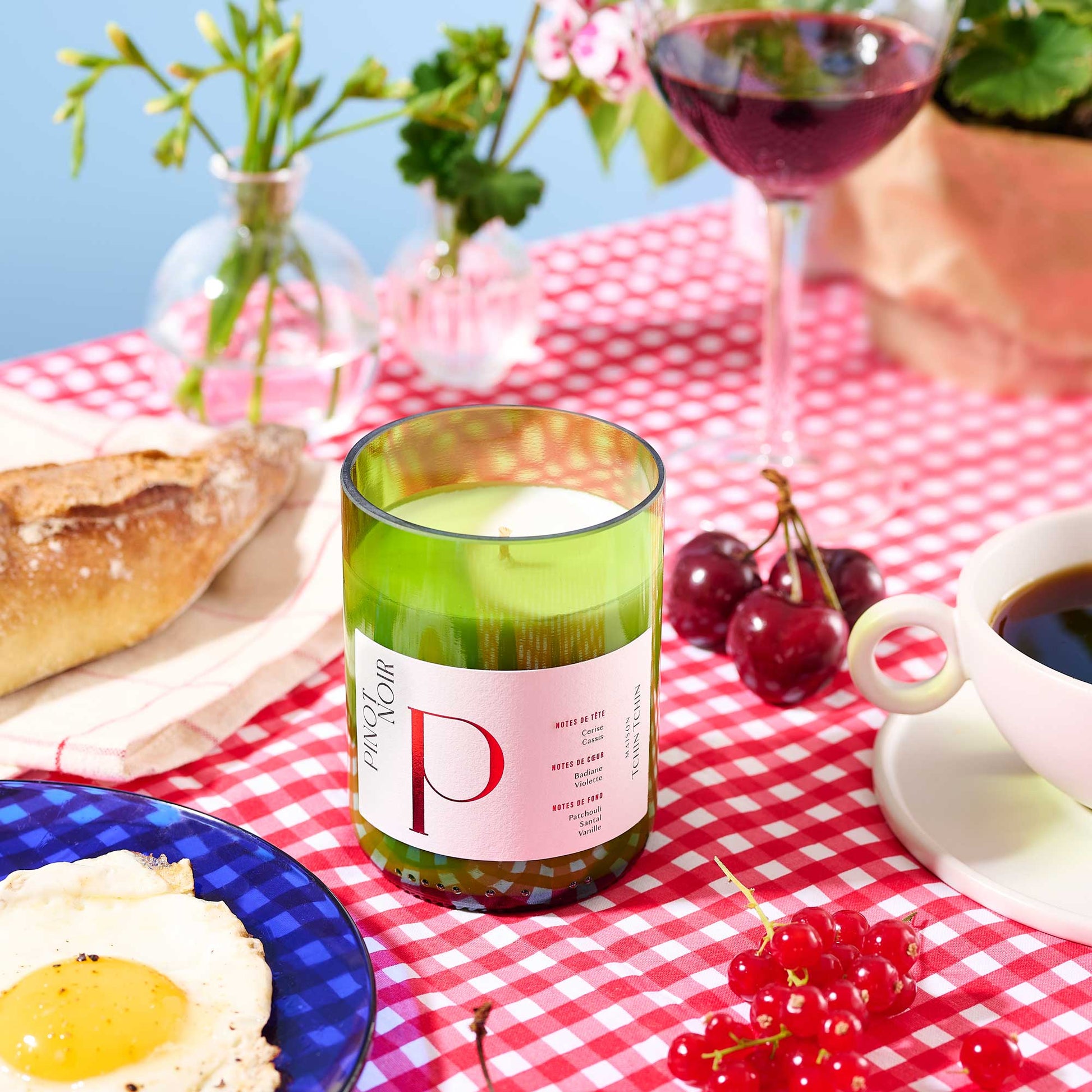 Bougie artisanale senteur pinot noir dans son flacon en bouteille de vin recyclé posé sur une table à côté d'assiette et de tasse de café