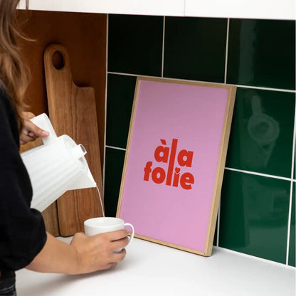 Affiche Papier and Co "à la folie" rose encadrée et posée sur le comptoir d'une cuisine