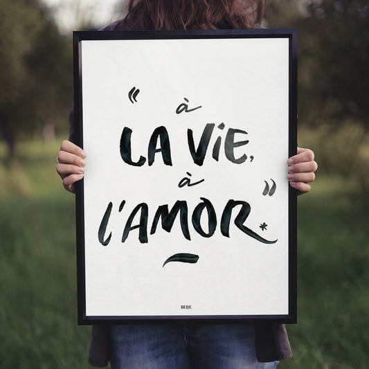 Femme portant un cadre avec l'affiche inscrite "À la vie, à l'amor"