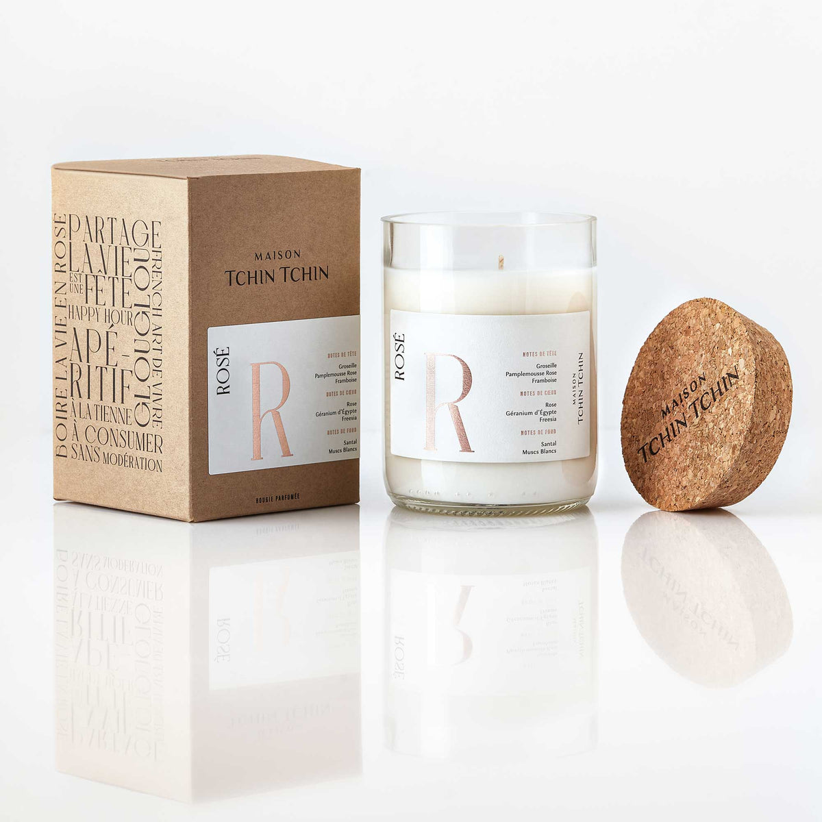 Maison Tchin Tchin Bougie parfumée au rosé posée sur un fond blanc avec sa boîte en carton recyclé.